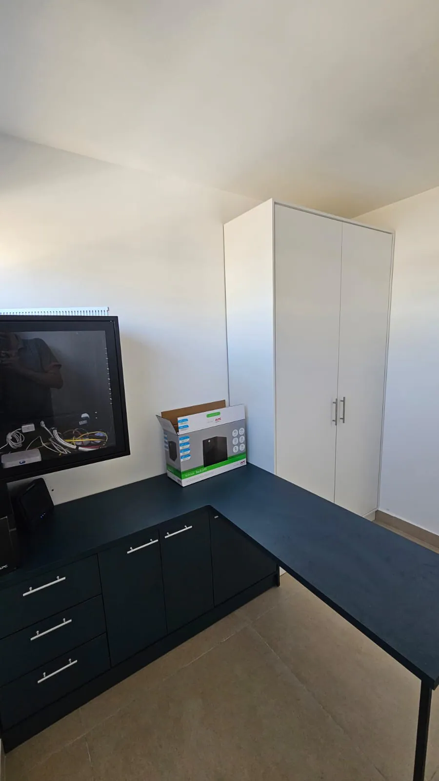 Home office com bancada e gaveteiro pretos e armário alto branco